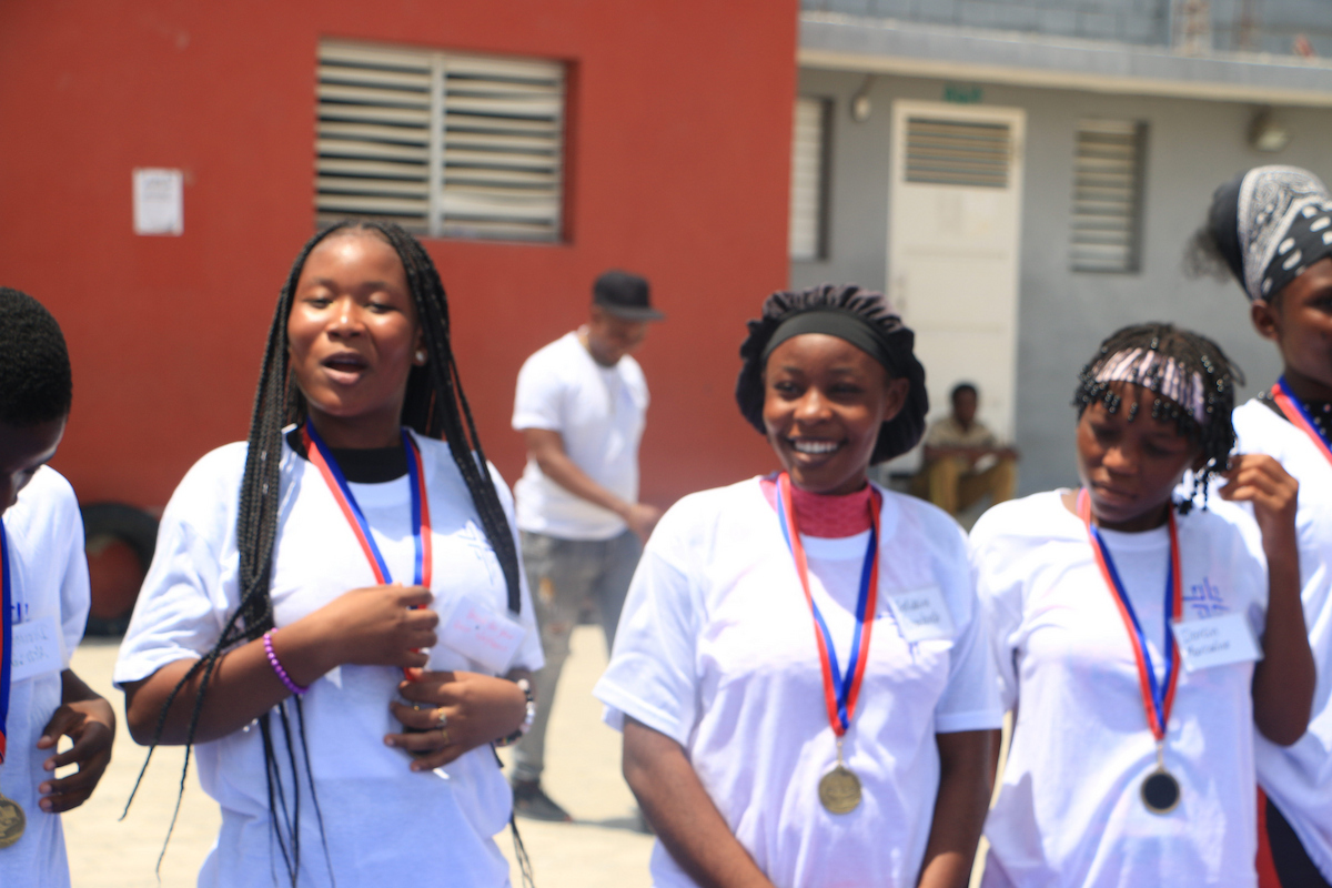 A group of young people wearing white shirts and medals stand together outdoors, smiling and posing for the camera.