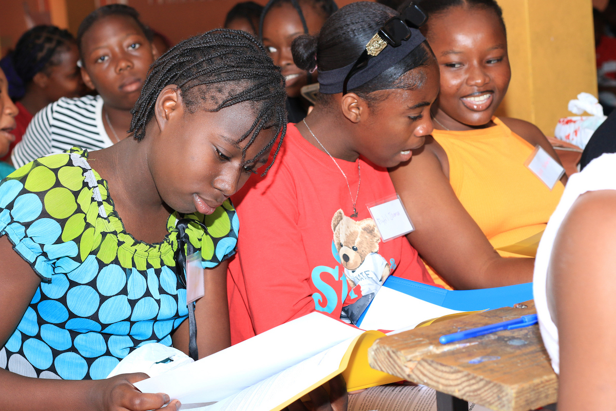 Several young individuals are seated at a wooden table, focused on reading or studying from open books.